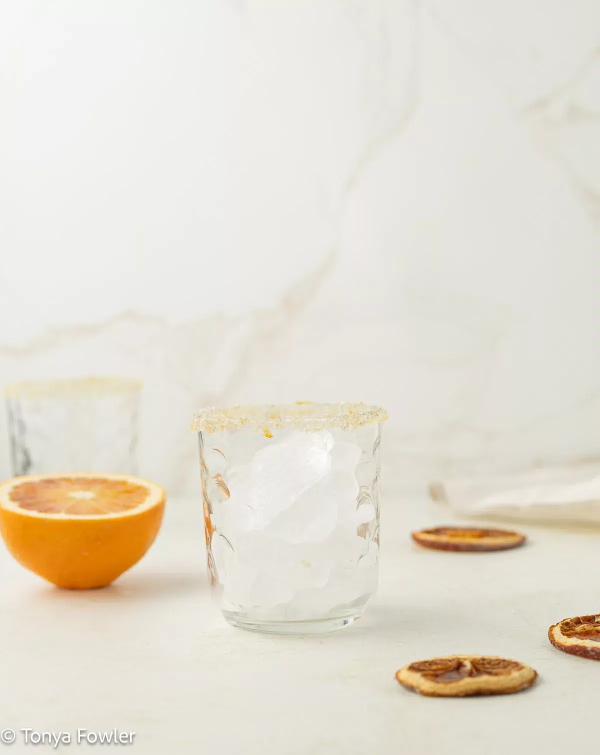 A cup with a sugar rim on a counter with blood oranges slices.