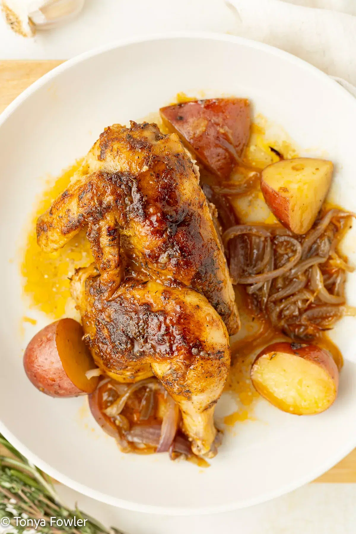 Half of a roasted cornish hen on a plate with potatoes and onions.