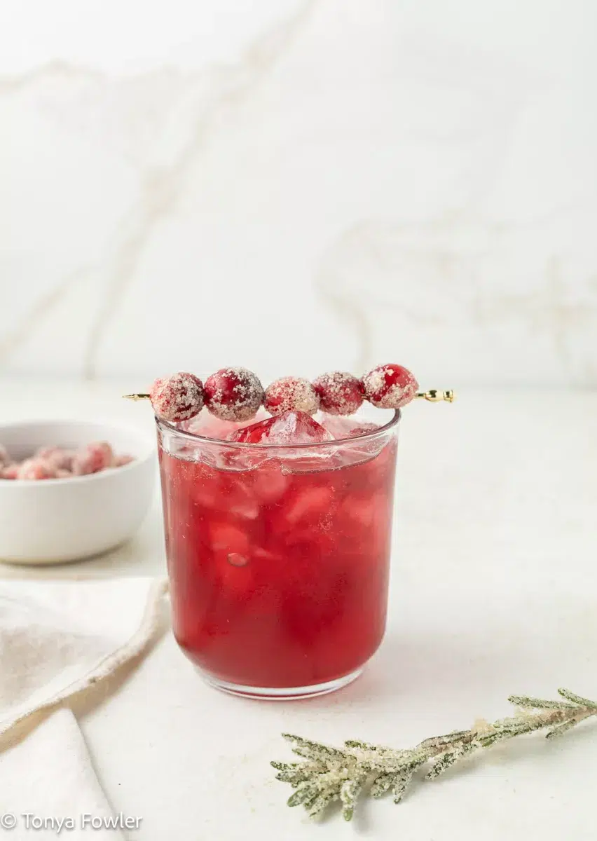 Cranberry Ginger Mocktail in a glass topped with sugared cranberries on a cocktail skewer.
