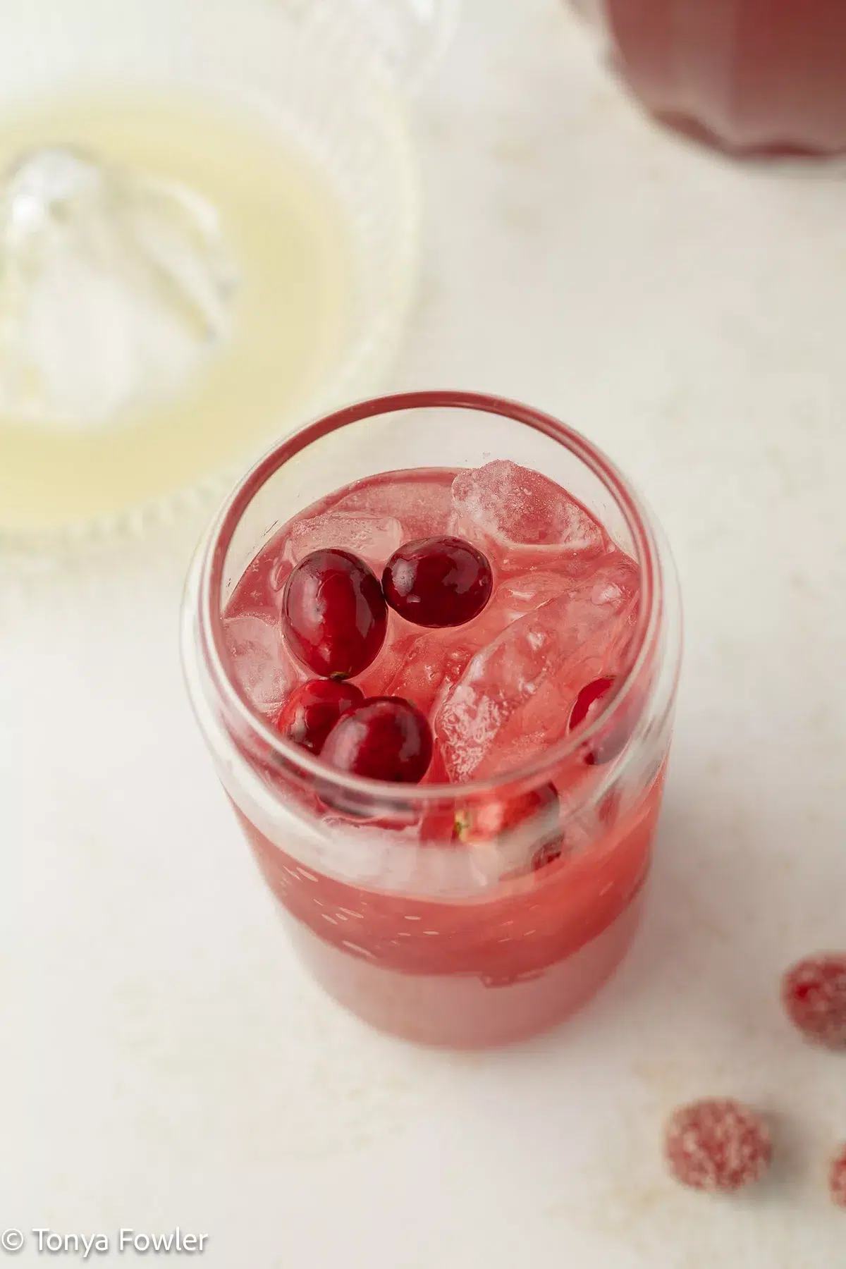3/4 overhead image of cranberry lemonade in a glass with fresh cranberries and ice.