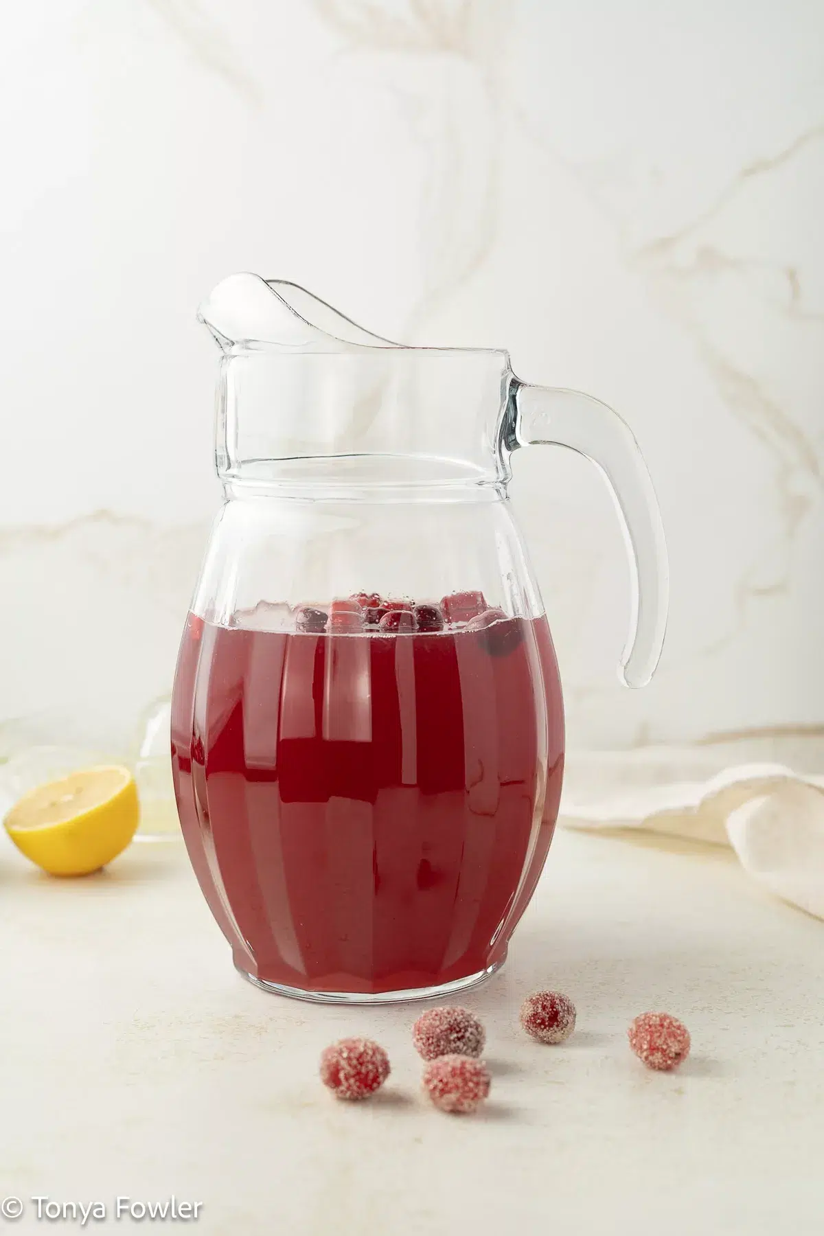 A pitcher of cranberry lemonade on a counter with sugared cranberries.
