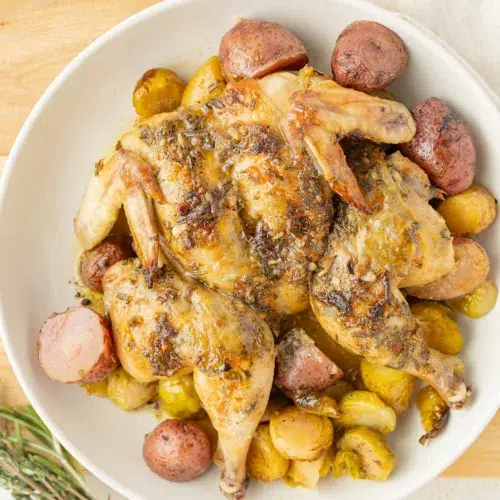 Herb butter cornish hen on a plate with potatoes and brussels sprouts.