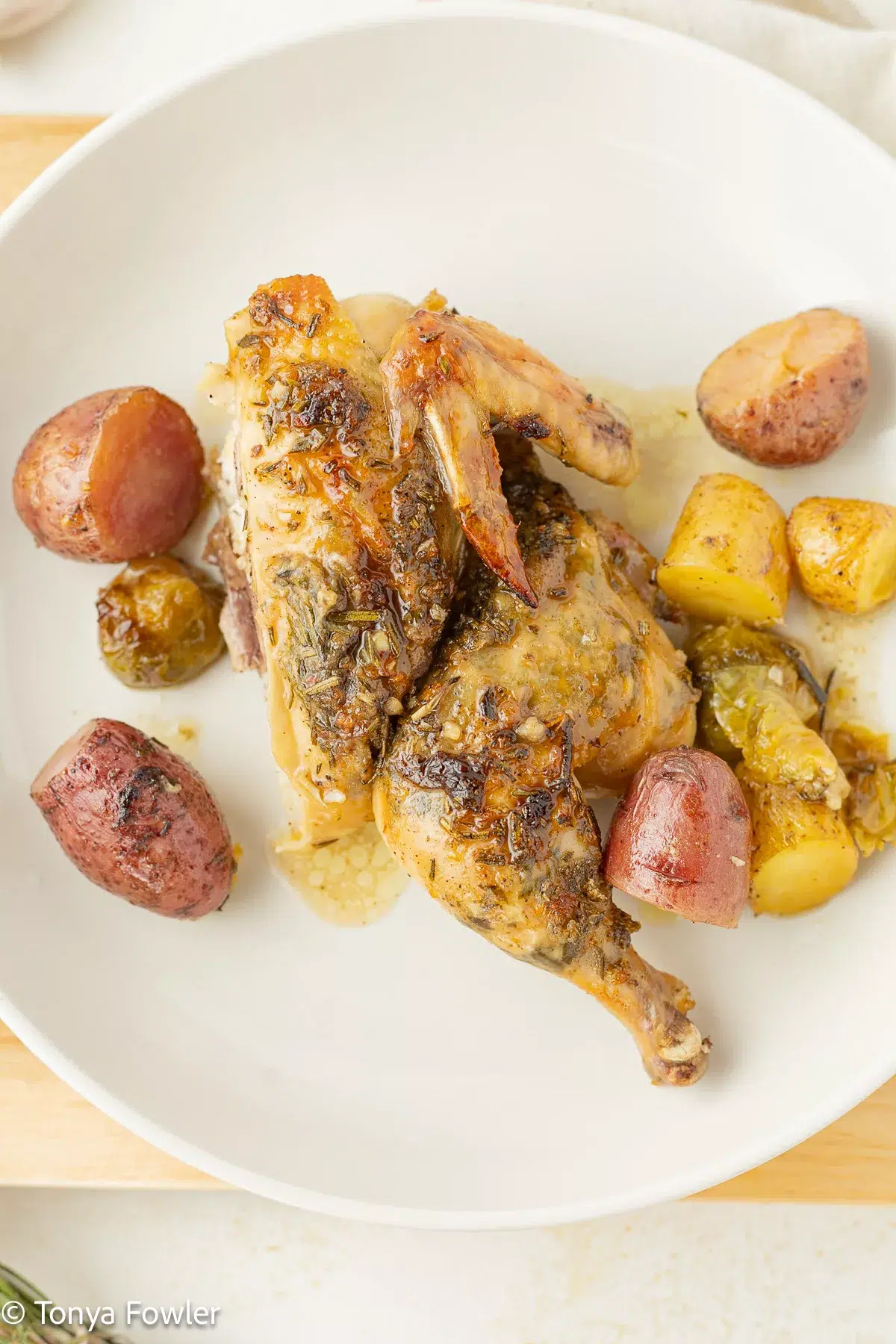 Half of a cornish hen on a plate with potatoes and brussels sprouts.