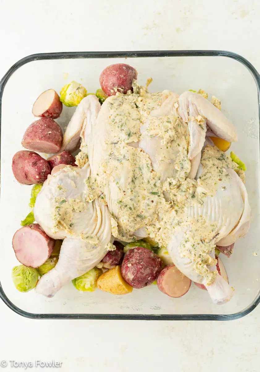 A spatchcock cornish hen topped with herb butter on a bed of potatoes and vegetables.