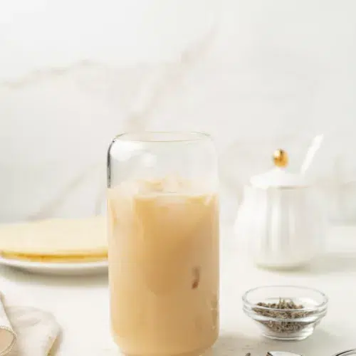 Iced lavender london fog in a glass with lavender buds on a counter.