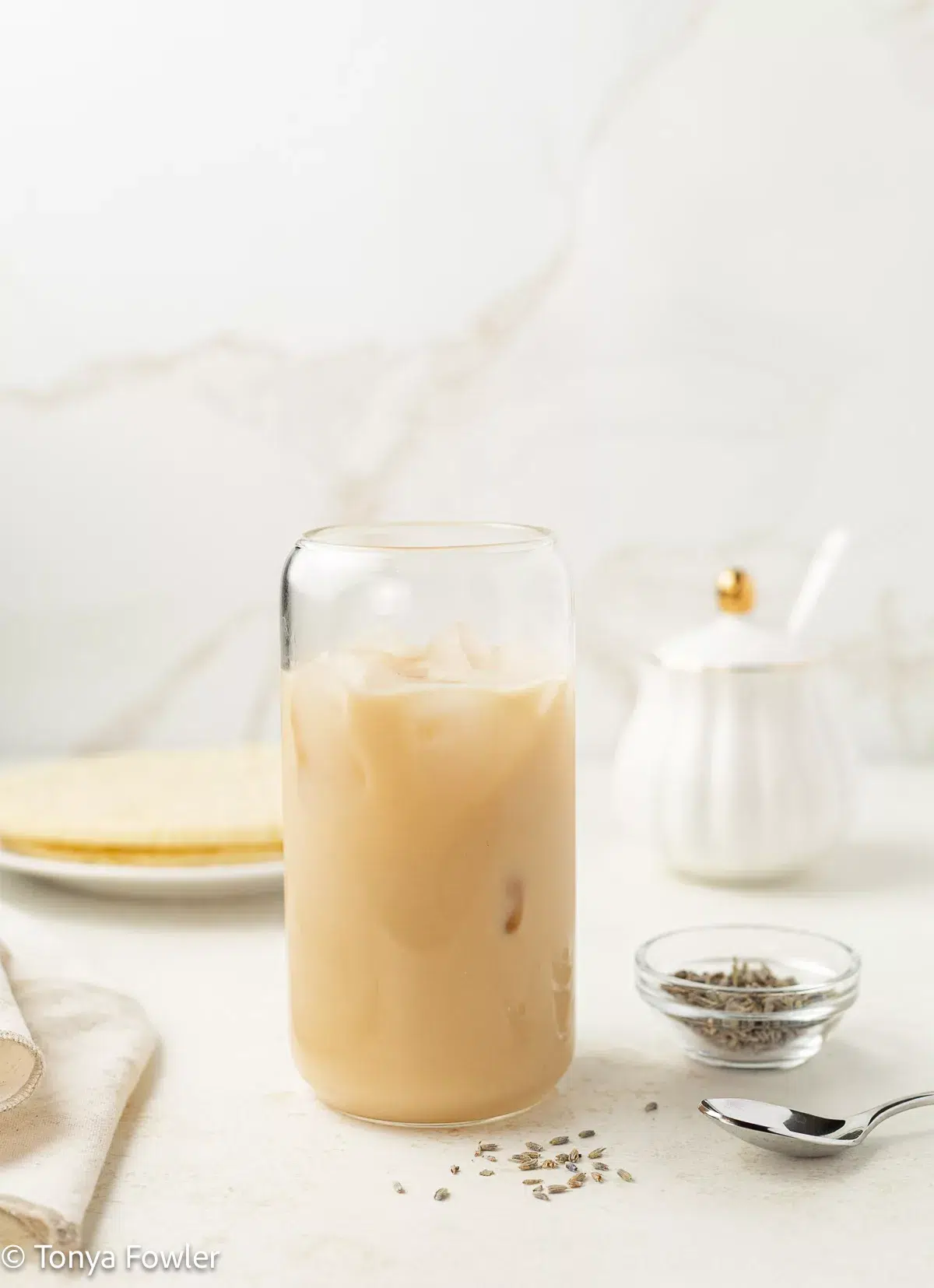 Iced lavender london fog in a glass with lavender buds on a counter.