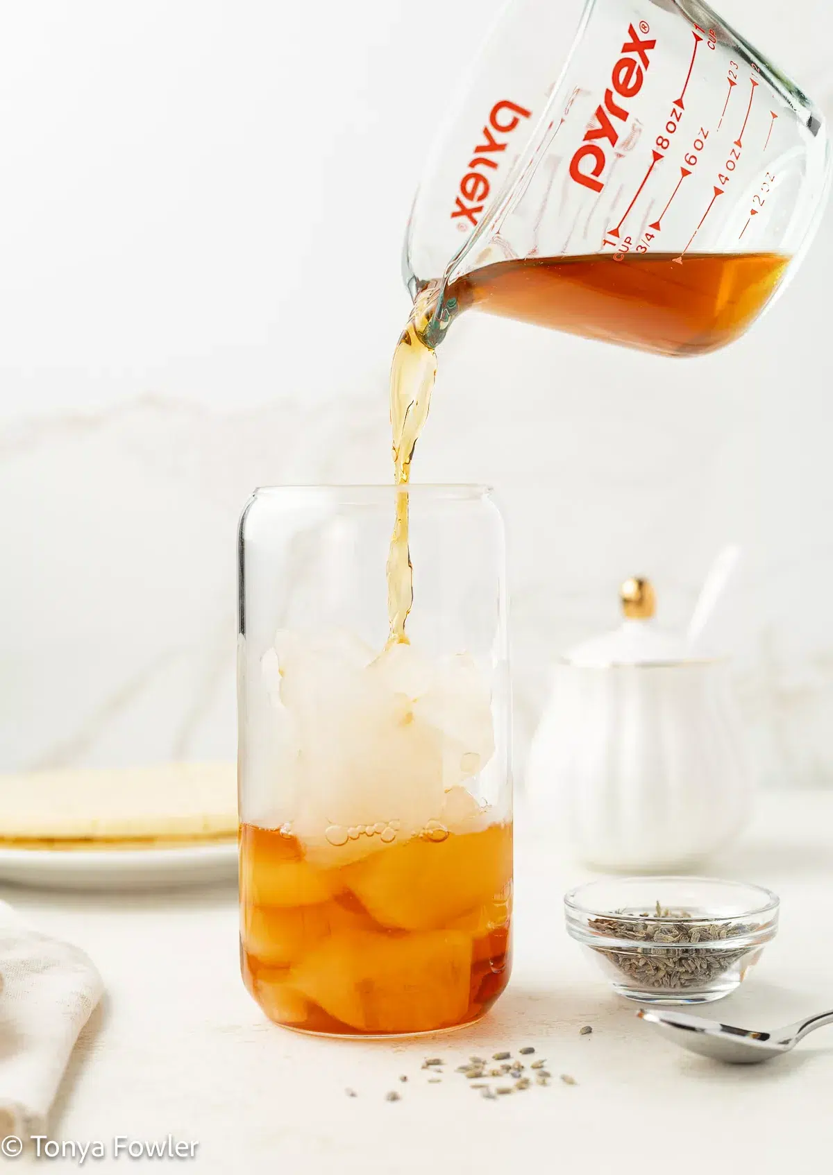Tea being poured into a glass with ice.
