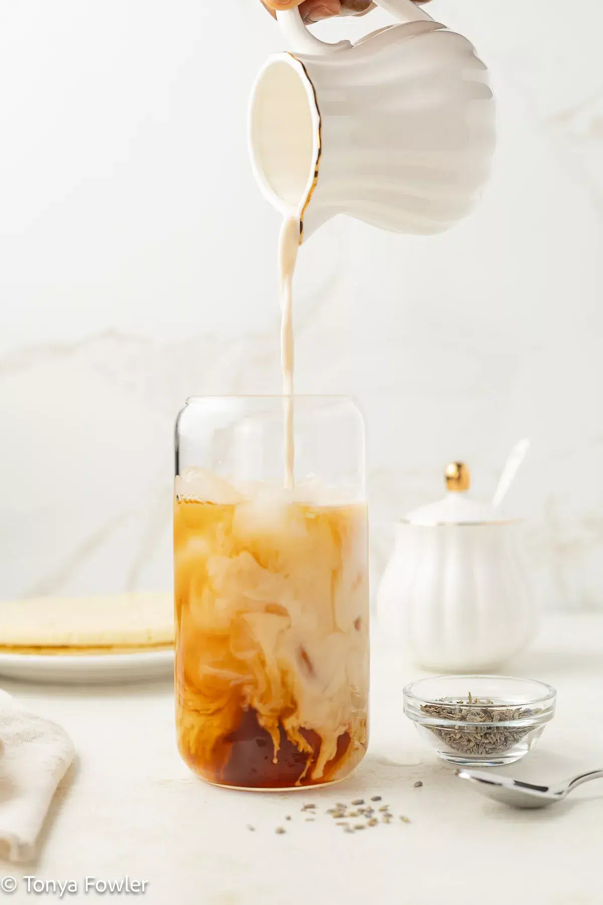 Milk being poured into a glass with tea and ice.