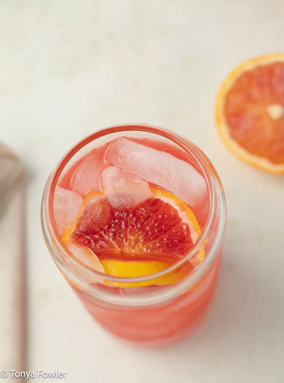 A 3/4 image of orange lemonade in a glass with oranges and ice.
