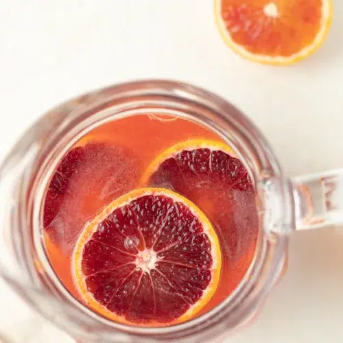 Blood orange lemonade in a pitcher with slices of blood oranges.