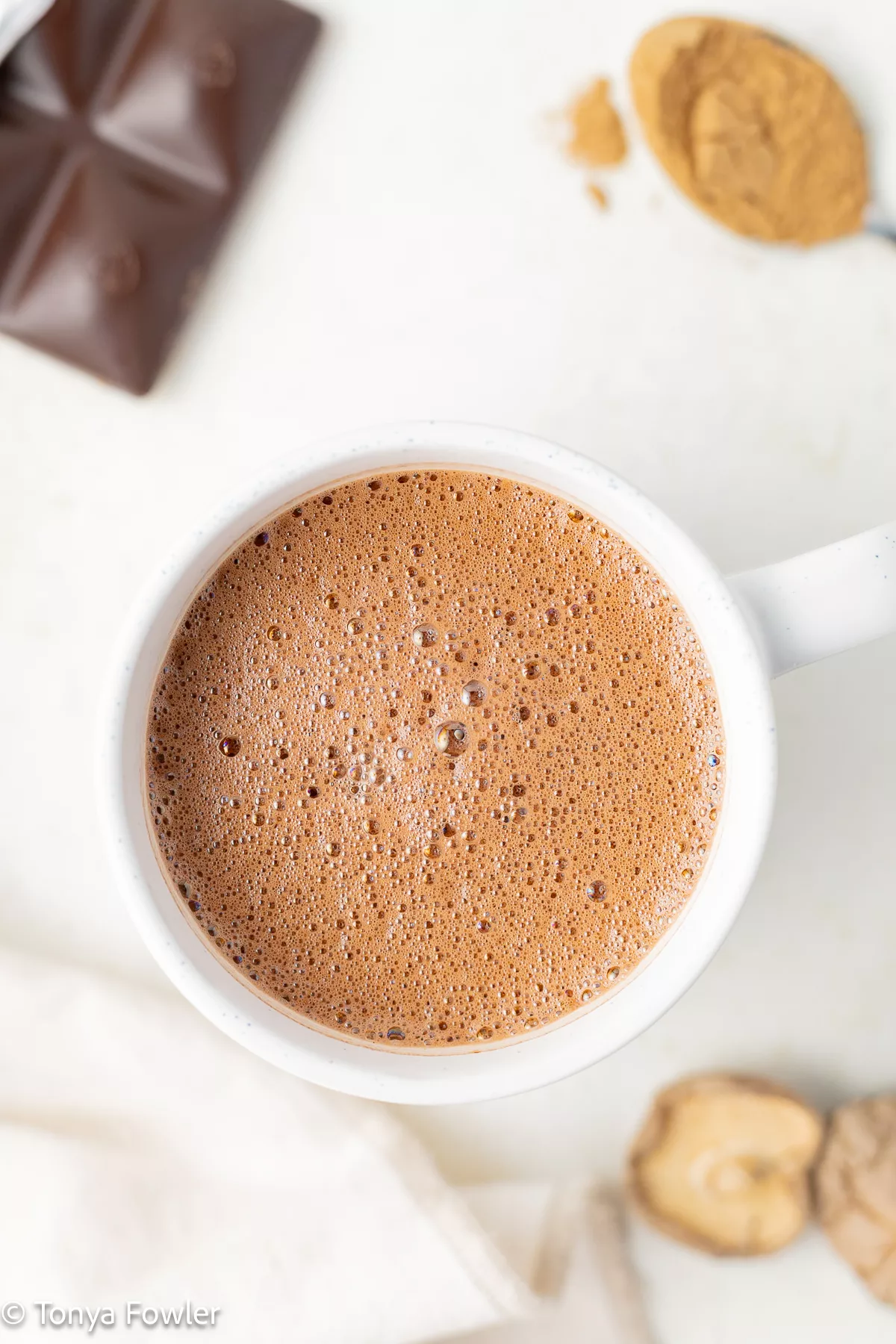 Overhead view of hot chocolate in a mug surrounded by a chocolate bar and mushrooms.