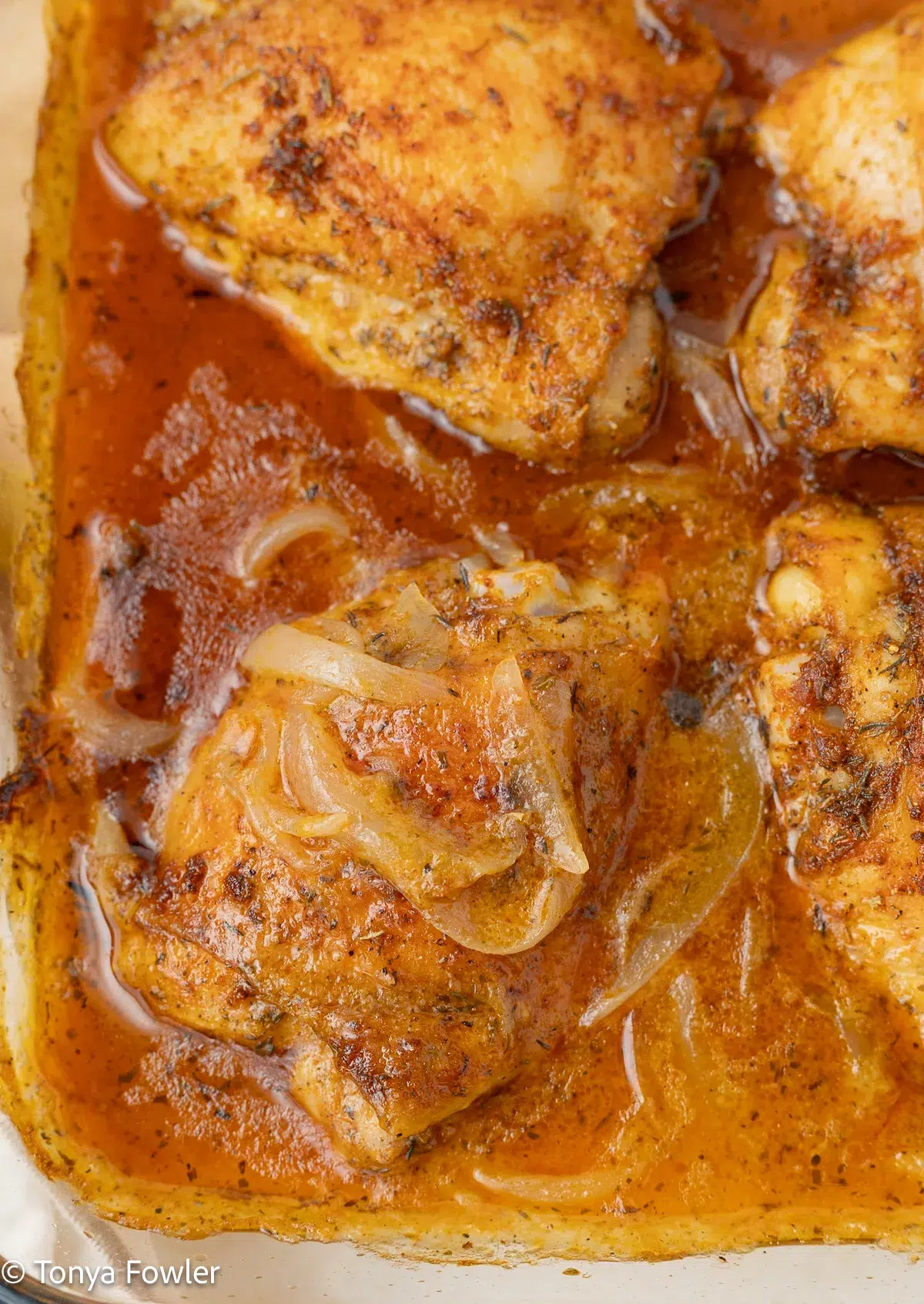 Smothered chicken thighs with onion gravy in a baking dish.