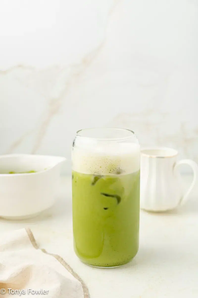 Matcha latte in a glass topped with protein milk.