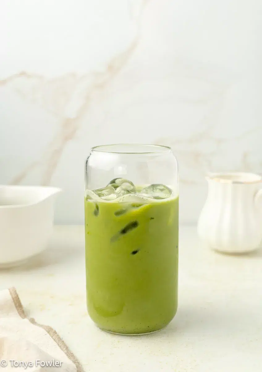Vanilla bean protein matcha latte in a glass with ice on a counter.