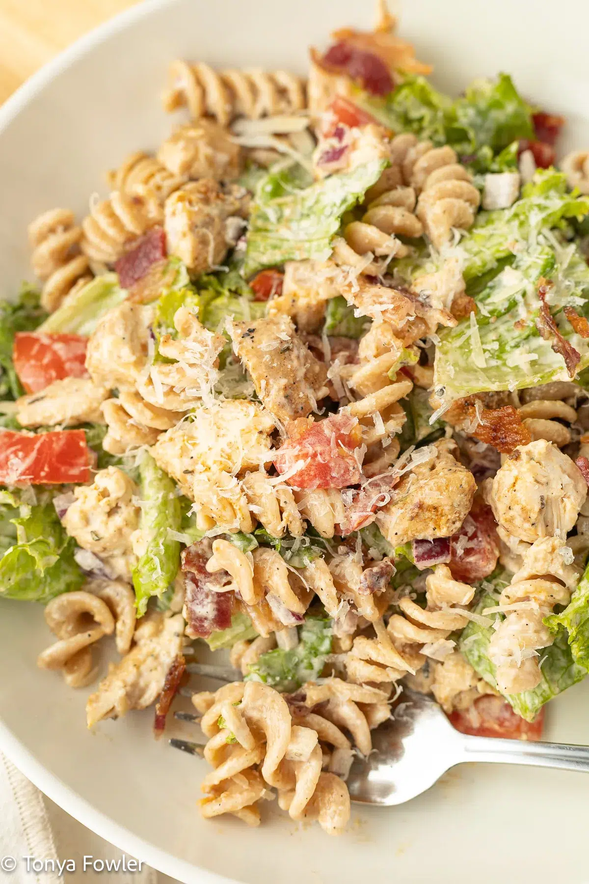 Close up image of chicken bacon caesar pasta salad on a plate with a fork.