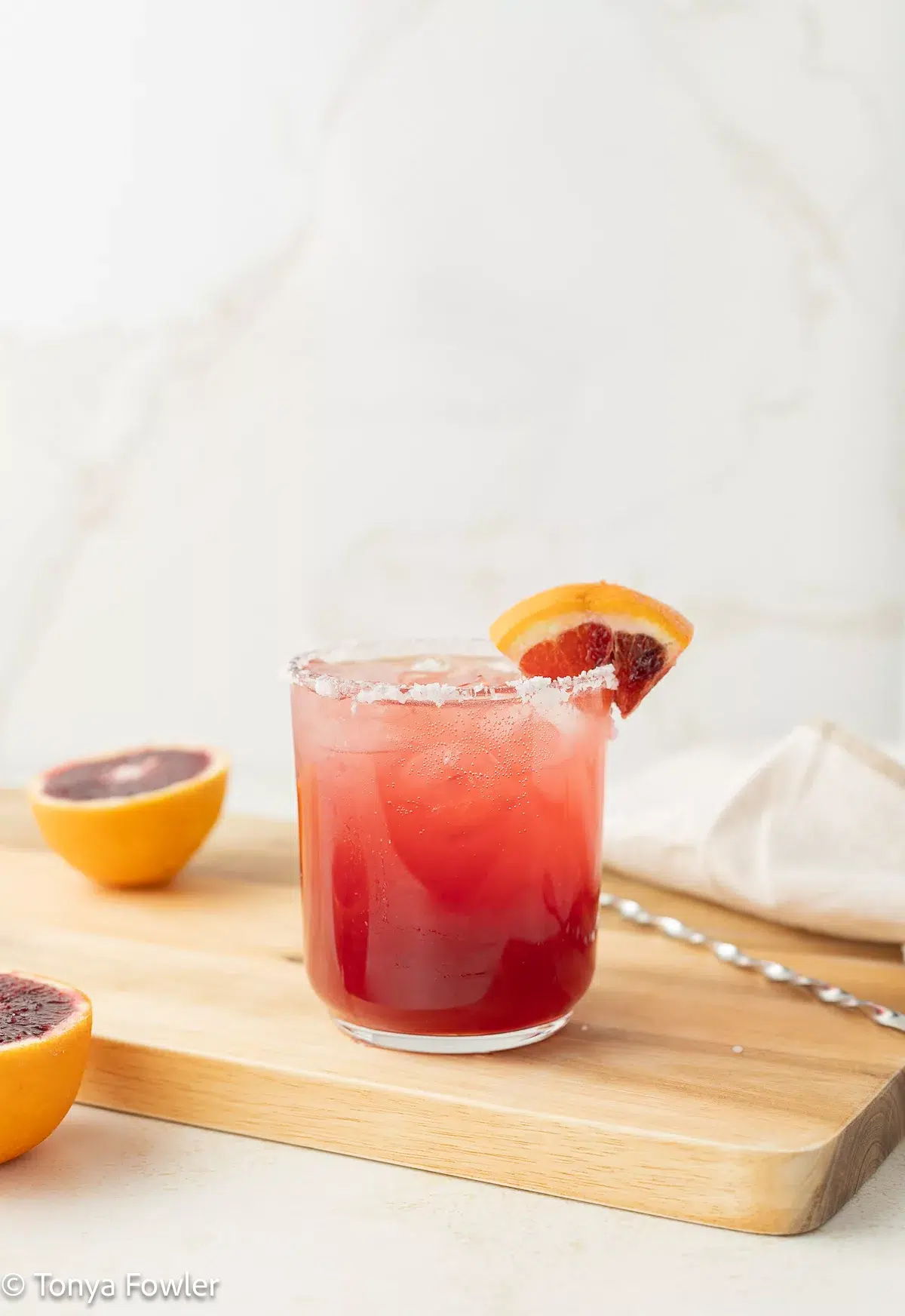 Straight on view of a blood orange paloma with a fresh fruit on the rim and counter.