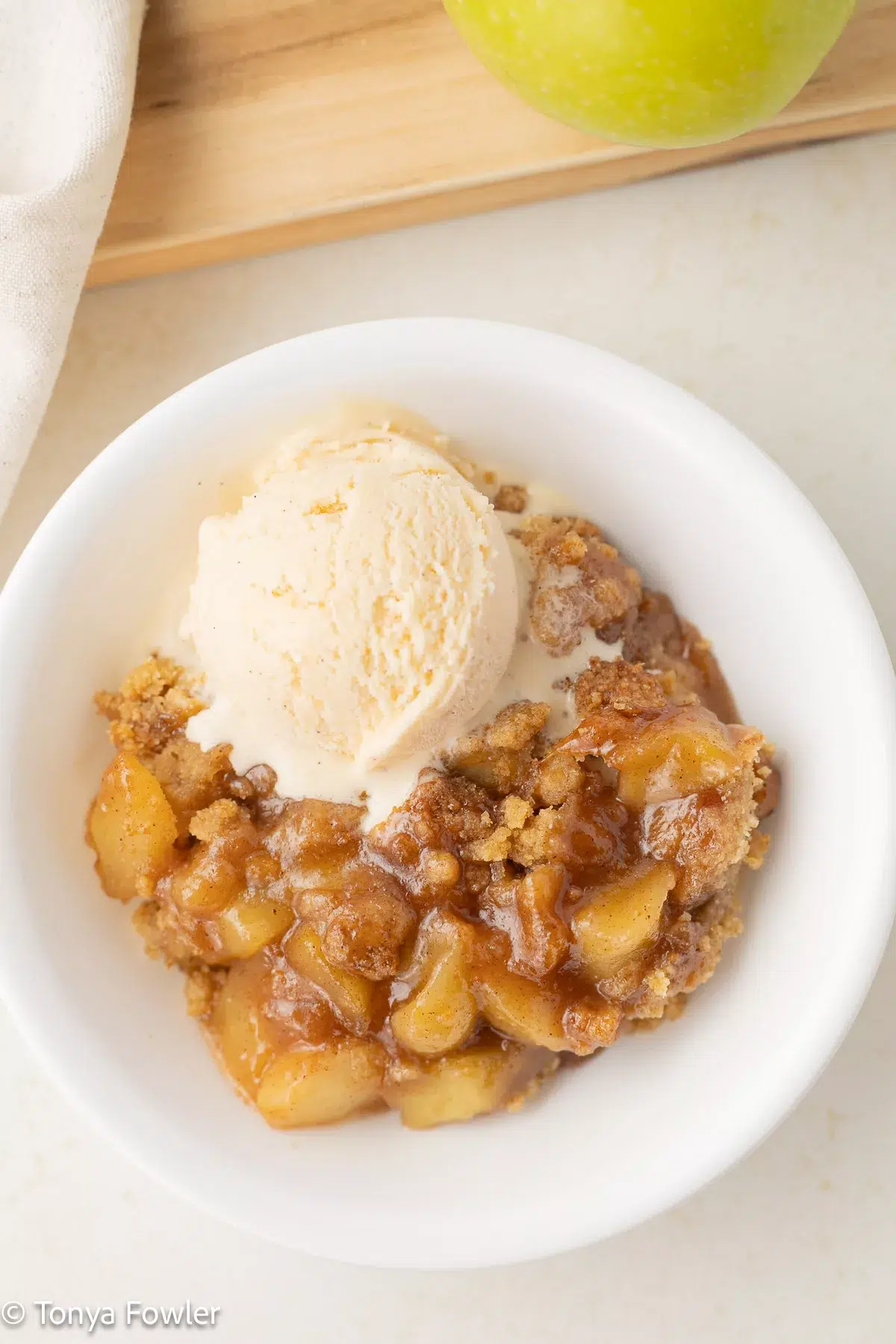3/4 image of an apple crumble topped with ice cream.
