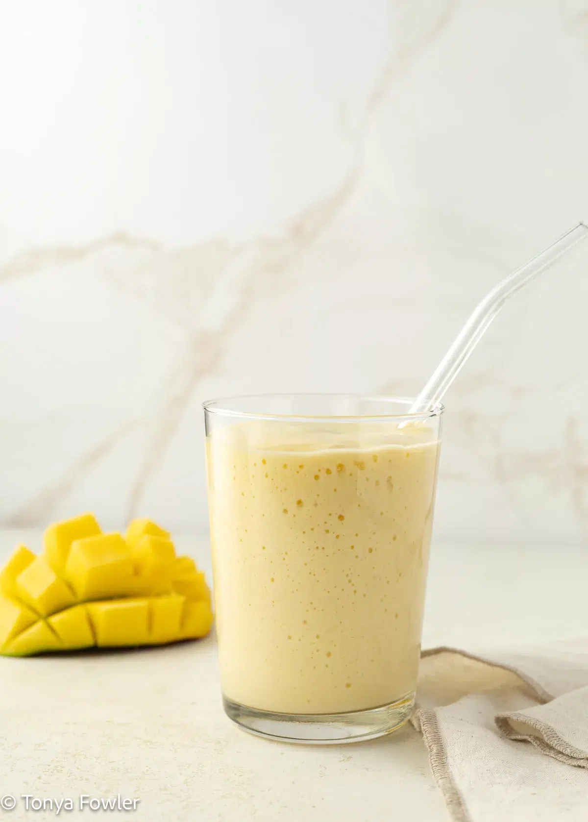 Mango kefir smoothie in a glass with fresh mango in the background.
