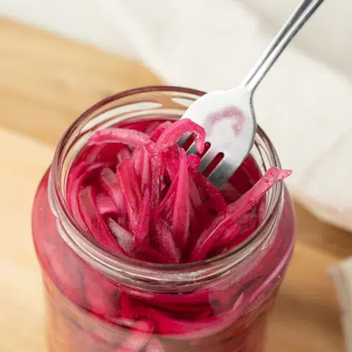 Pickled red onions in a jar with a fork.