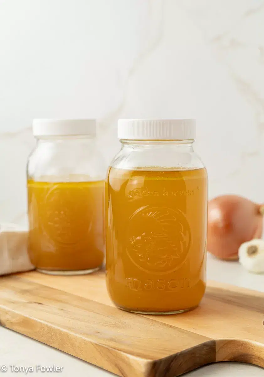 Chicken broth in a mason jar sitting on a cutting board.