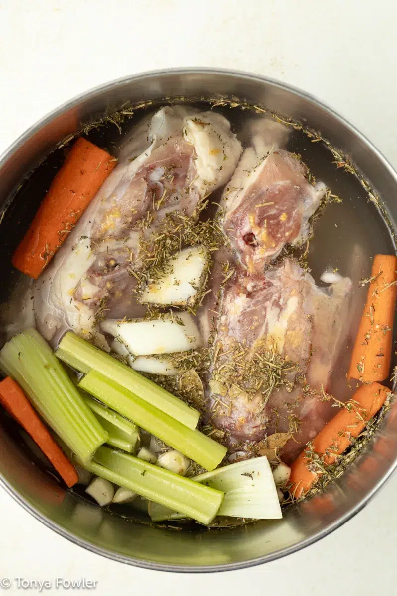 Raw chicken backs in a pot with vegetables and seasonings.