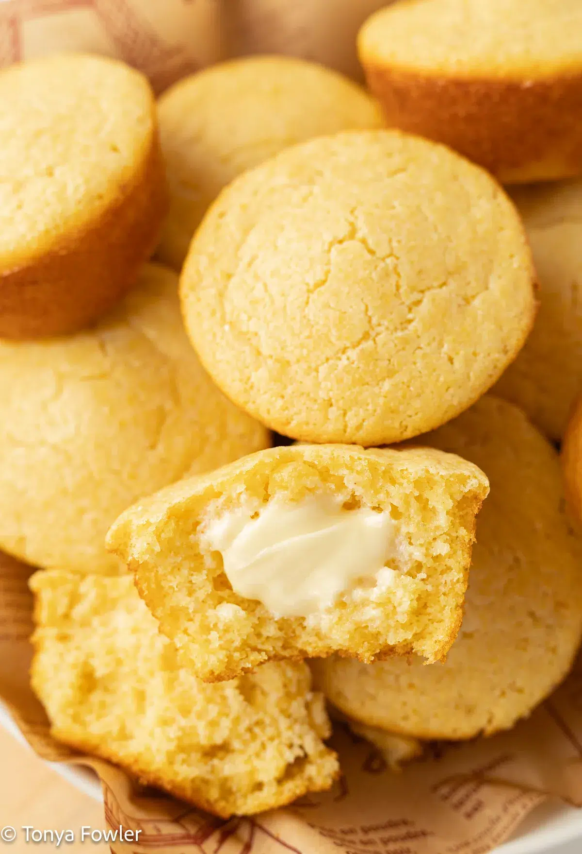 Close up image of a Cornbread muffin sliced open spread with butter.